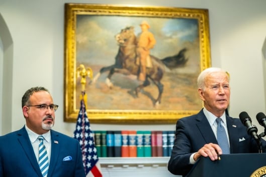Education Secretary Miguel Cardona stands next to President Joe Biden in the Roosevelt Room of the White House