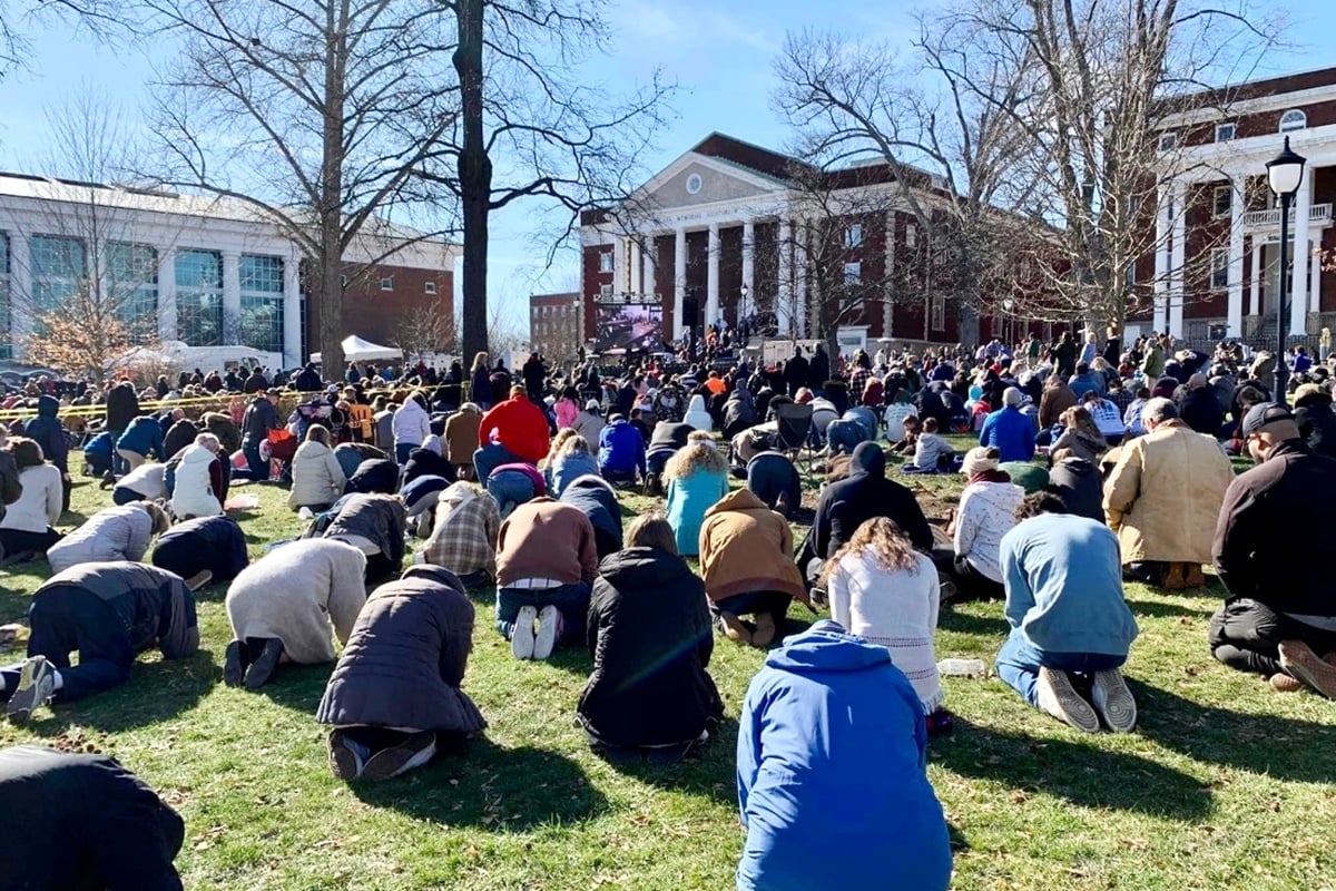 Students and visitors kneel on a lawn at Asbury University.