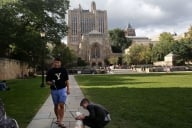 A student in a Yale sweatshirt walks a dog on campus while another pets it