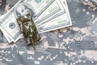 Money on top of a military uniform with a toy tank on both