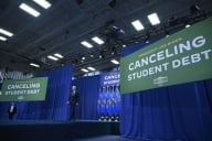 President Biden walks on a stage in front of signs that read “Canceling Student Debt.”