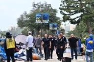 Police walk under a blue “Go Bruin” banner as crews clear away an encampment at the University of California, Los Angeles