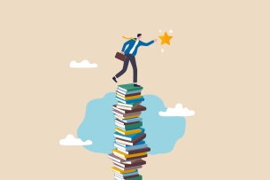 Man holding a briefcase and reaching for a star stands atop a very tall stack of textbooks