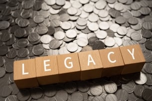 Wooden blocks spelling “LEGACY” sit atop a pile of shiny coins.