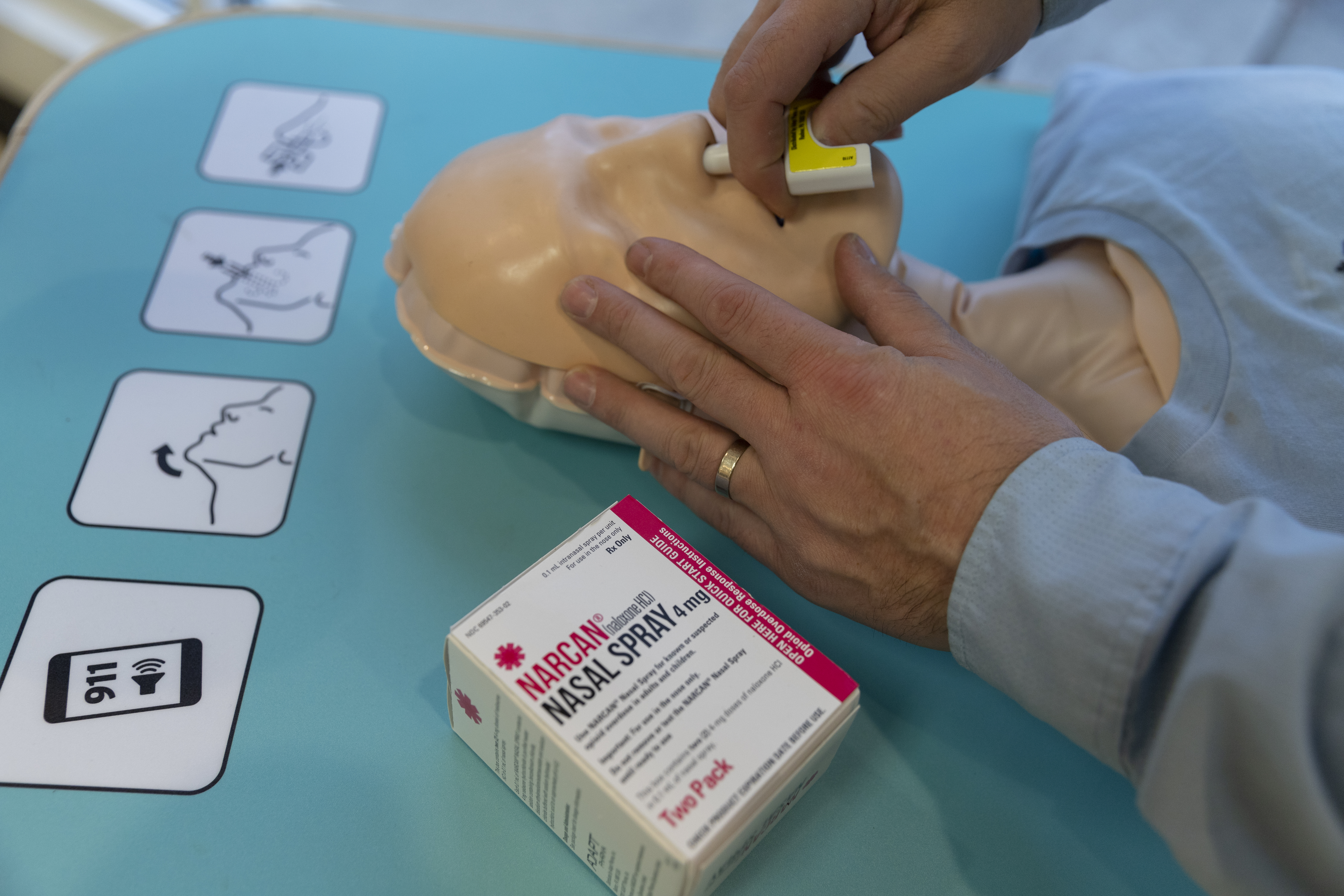 Close-up of the head of a training dummy, with a person demonstrating how to administer the NARCAN nasal spray.