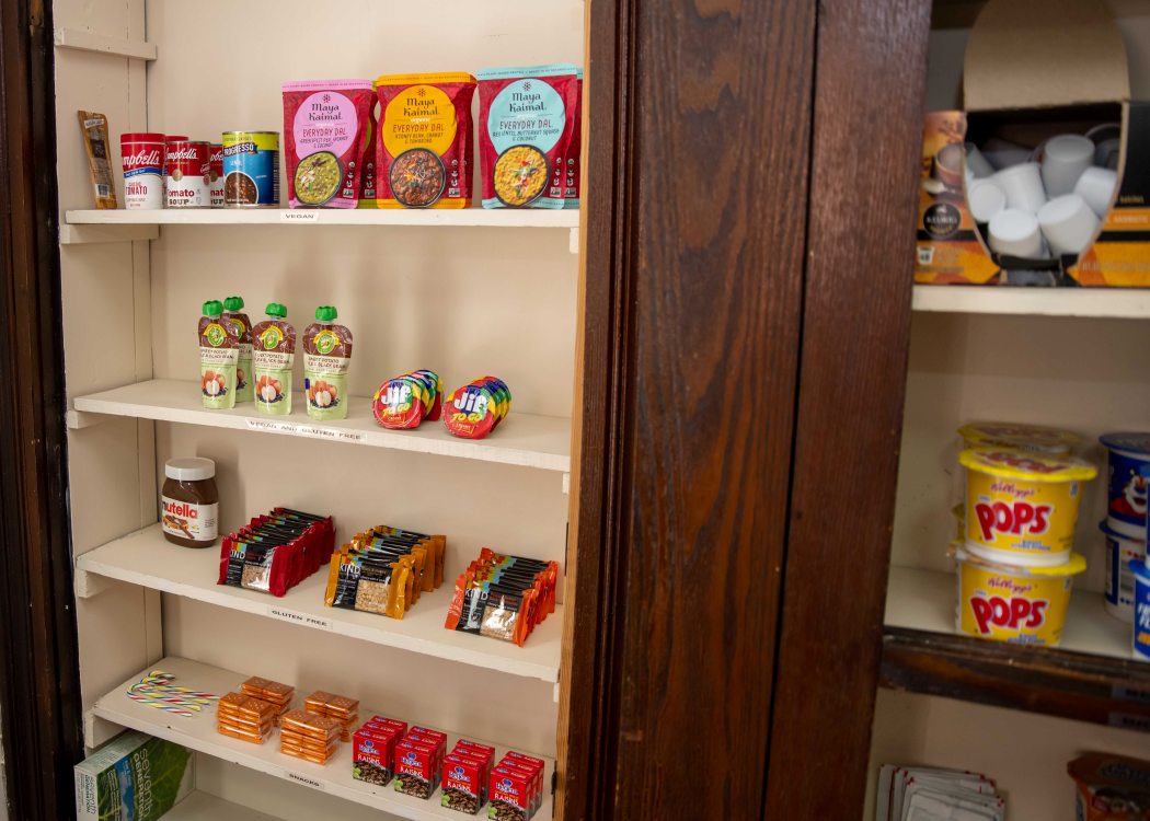 A shelf in the Campus Cupboard featuring items like breakfast bars, Nutella, instant rice, apple sauce, peanut butter, cereal and coffee.