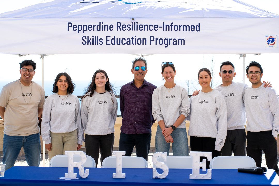 A group of students and staff stand under a Pepperdine RISE pop-up tent for a campus event.
