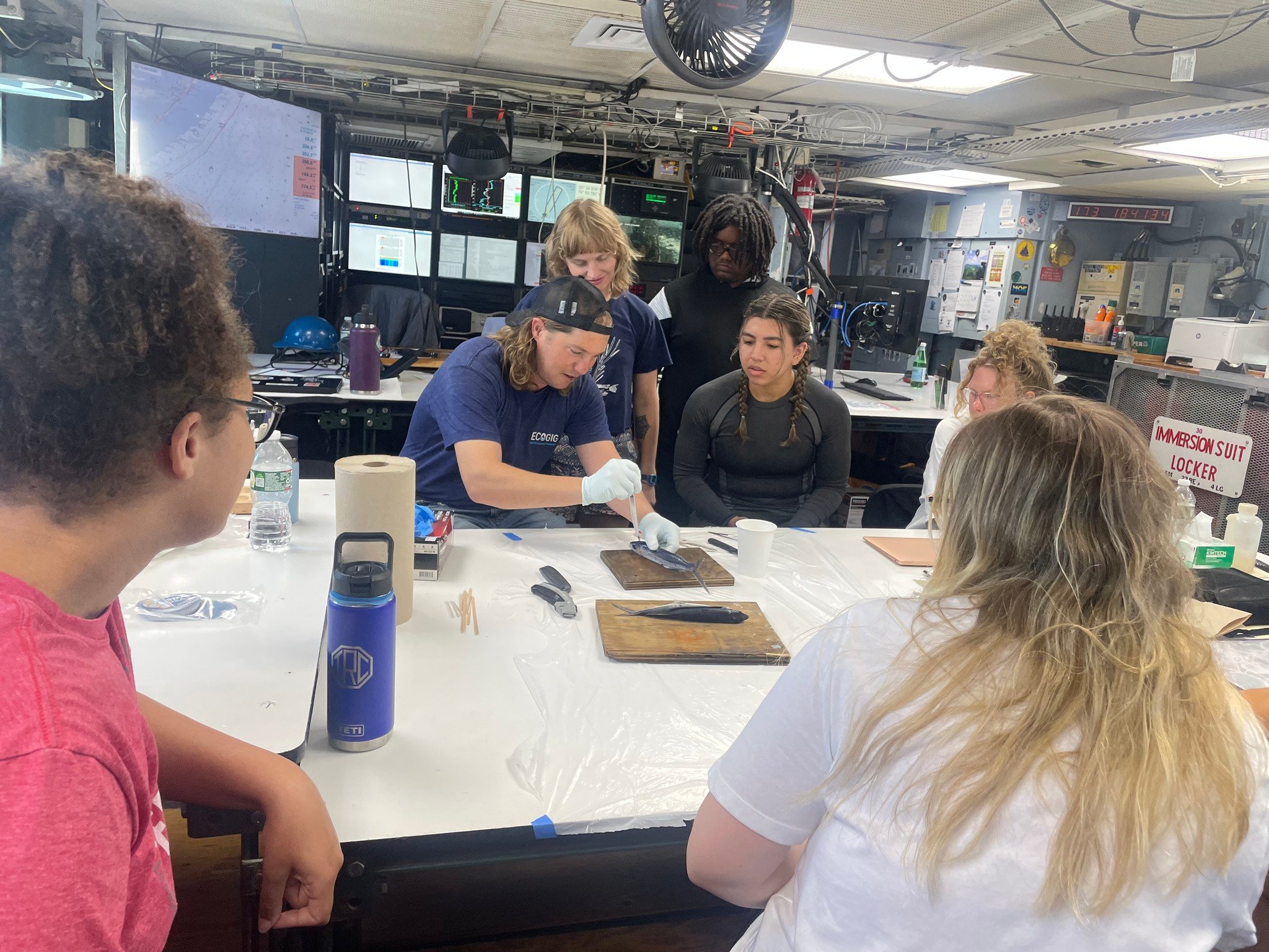 Students sit around a white table dissecting two fish.
