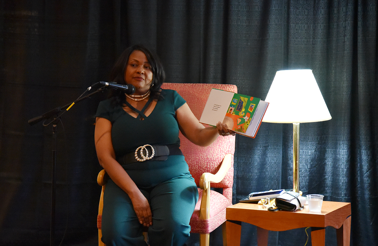 Hollins president Mary Dana Hinton reads Goodnight Moon to students in the campus student center, sitting in a pink armchair illuminated by a white lamp.