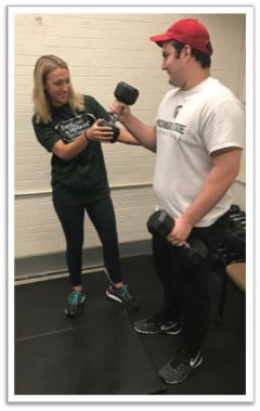 A kinesiology student helps a peer use dumbbells in an ACTIVE Spartan session.