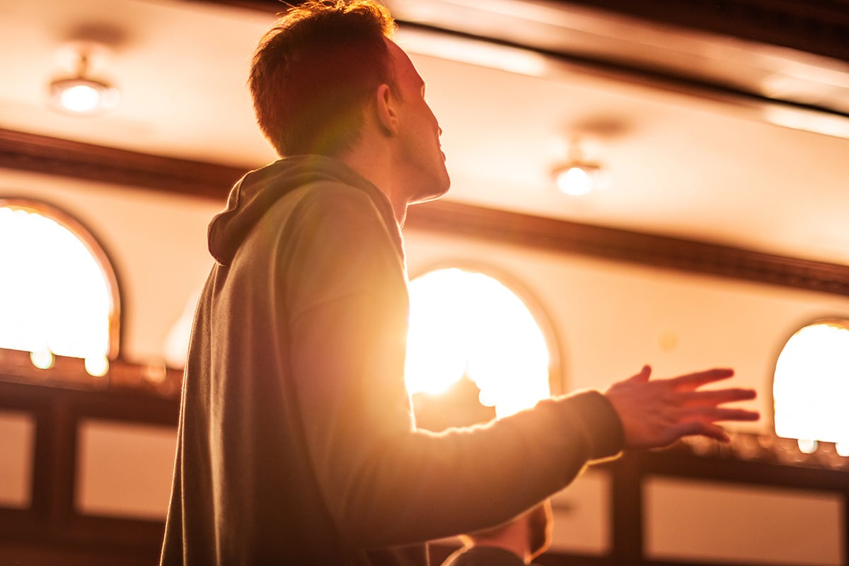 One Asbury University student closes his eyes and raises his hands while standing in the campus chapel.