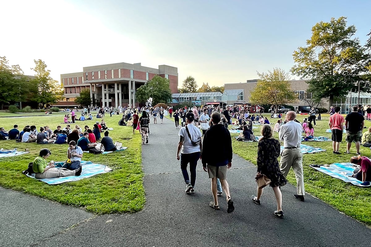 A wide shot of the Hampshire campus, with hundreds of people walking around and sitting on the grass.