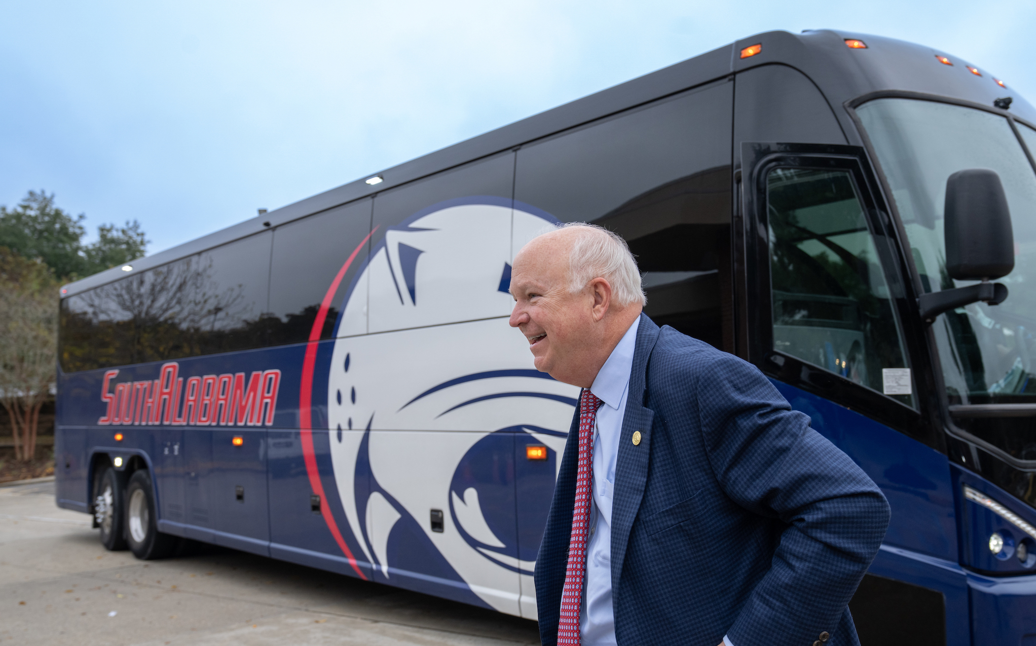 A smiling president Jo Bonner standing in front of a coach bus that says South Alabama.