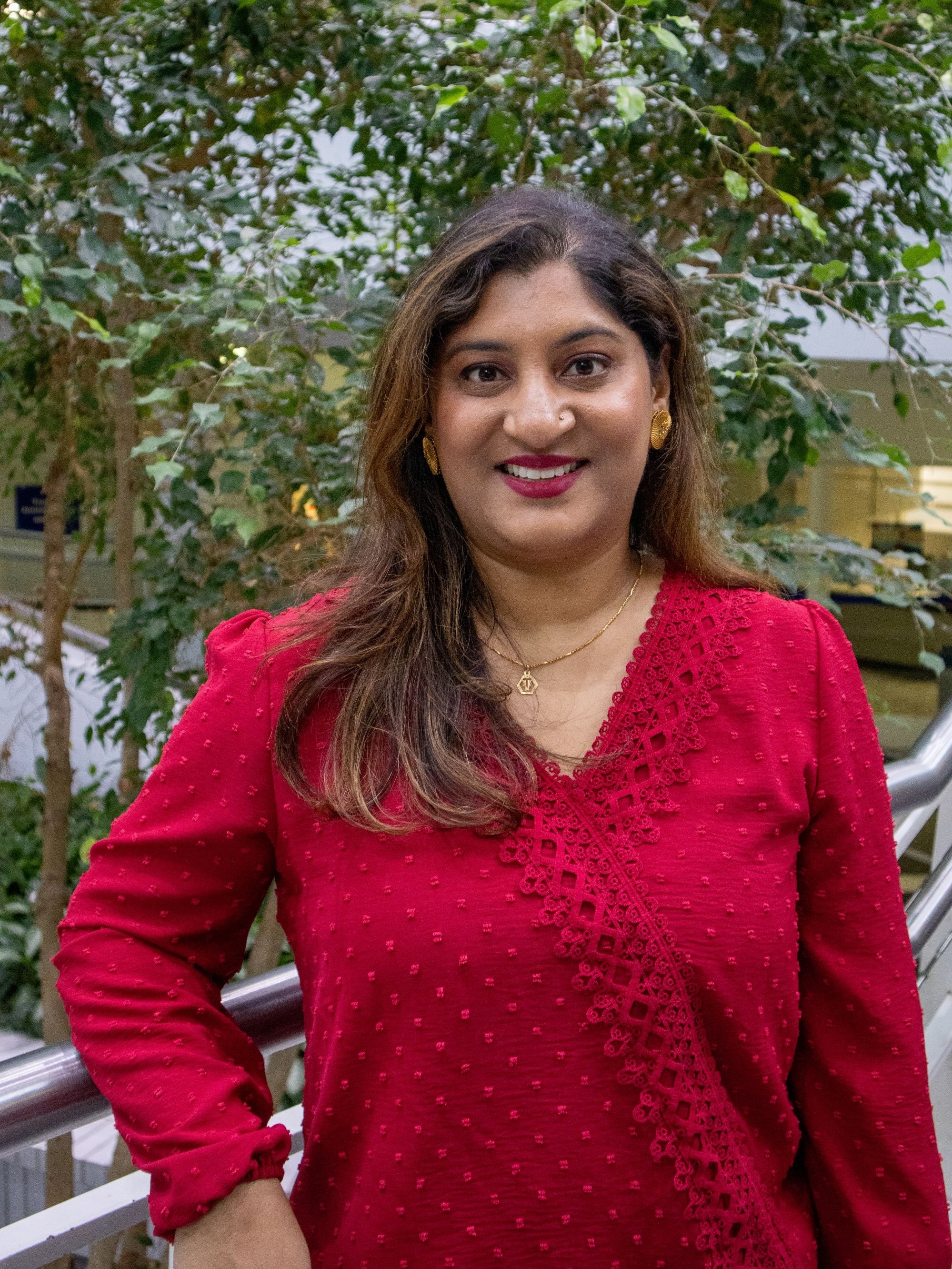 Viraj Patel smiles for a headshot wearing a red blouse in an outdoor space.