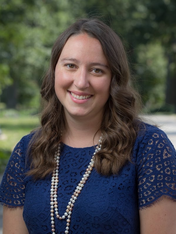 Katie Clark smiles for a headshot wearing a blue blouse and silver necklace