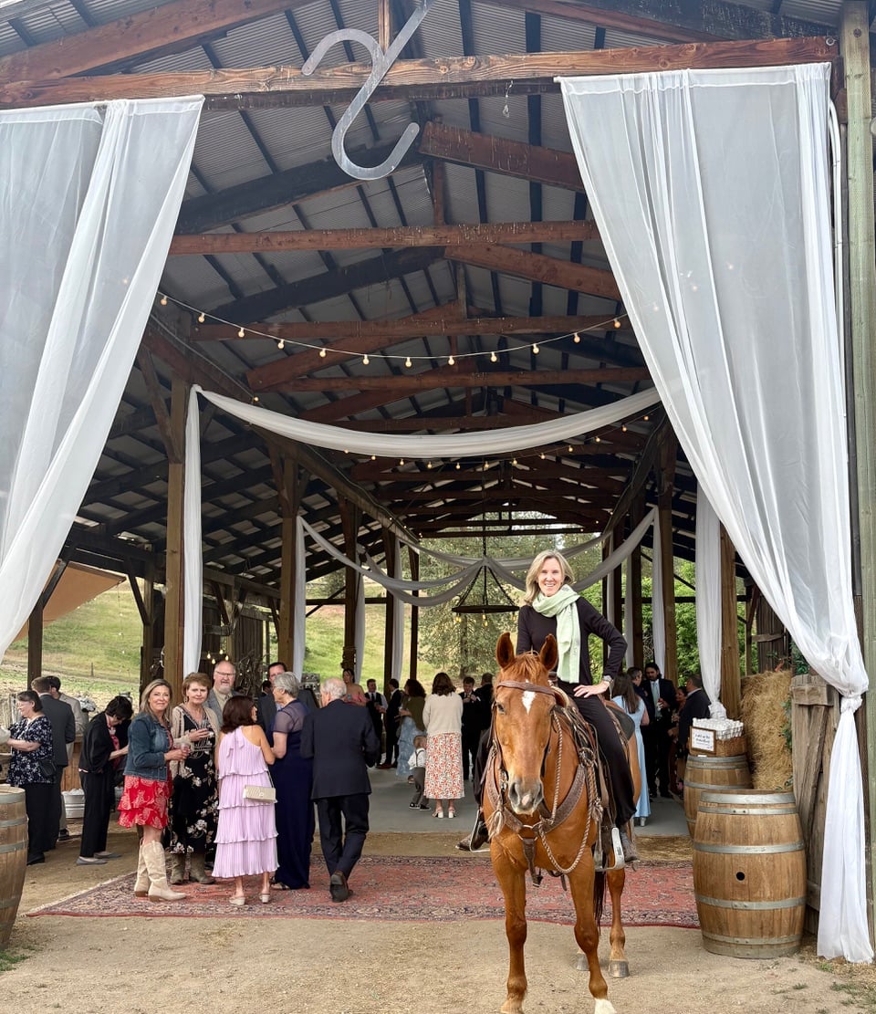 Rachel Toor on a horse, in front of a pavilion decorated for a wedding.