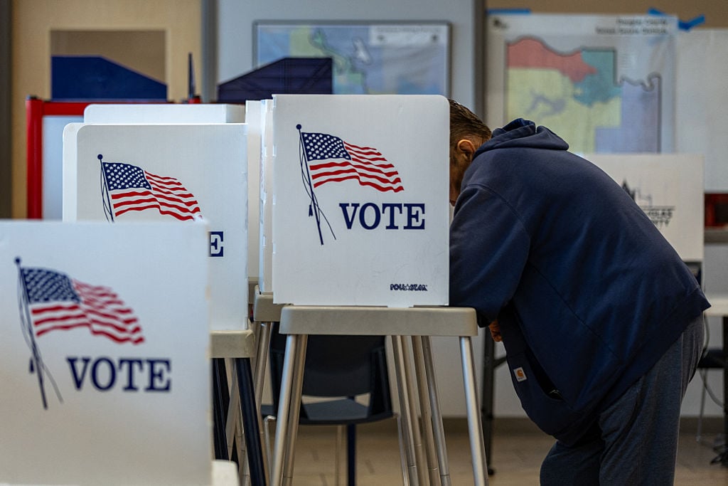 A person leans behind a white tabletop placard that says Vote with an American flag above it.