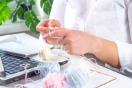 hands knitting over a computer with a ball of yarn to one side