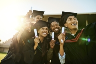 Five college students smile in academic regalia, holding their paper diplomas.