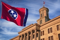 The red and blue Tennessee state flag flies in front of the state capitol building.
