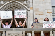 Four Pitt students stand on a balcony holding placards protesting the administration's slow response in notifying them of a reported active shooter threat.