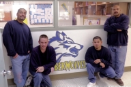 Four incarcerated students stand in front of a mural of the Blue Mountain Community College logo at Eastern Oregon Correctional Institution.