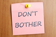 The words "Don't bother" written on a pink note tacked to a wooden door. 