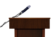 A wooden speaker podium and microphone, against a white background, with no speaker behind it. 