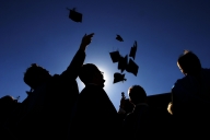 A group of graduates in silhouette tosses their caps into the air against a blue sky.