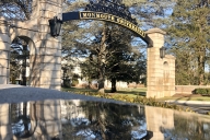 An arching sign reads "Monmouth University" and is reflected in water in the foreground