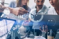 Four businesspeople examine a data visualization on a virtual screen.