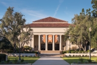 A building with neoclassical columns on a campus green lined with trees