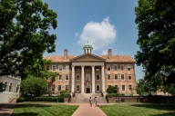 An neoclassical brick building stands in the middle of a tree-lined college campus