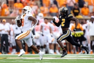 Two football players running, one in front with a ball.