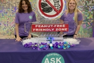 Two Duke Dining staff members smile at a table featuring a peanut-free friendly zone ice sculpture to share the launch of the Ask Me program. 