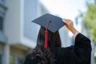 A woman stands with her back to the camera holding her graduation cap.
