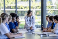 A group of nursing students sits around a long conference table looking at the instructor