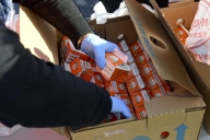 A photo of gloved hands sorting through a box of orange juice cartons.