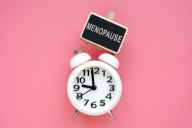 A sign with the word "menopause" above an alarm clock, against a pink background.