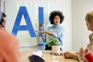 A woman points at large letters that spell out "AI"