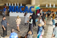 People walk past a sign that says NACAC in a convention center hall