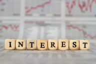 Block letters that together spell "Interest," against a backdrop of line graphs.