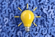 Bright yellow lightbulb sitting on a sea of blue question marks