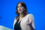 A brown-haired woman at a podium in front of a blue screen