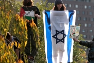 Three protesters, one for Israel and two for Palestine, stand by greenery.