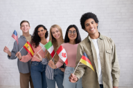 A group of five college-aged students holding flags from five different nations.