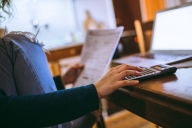 Close-up of a young woman using calculator, laptop and analyzing documents