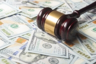 A gavel sits on a pile of one-hundred-dollar bills