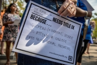 A person holds a sign on white paper that says "My alma mater needs Title IX because women and everyone deserve to attend a college free from sexual predators."