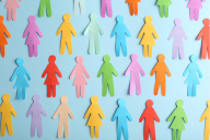 A collection of human cut-out paper figures of varying colors and genders placed flat against a blue background, illustrating the concept of diversity.